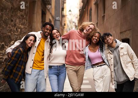 Group of twenties people looking at the camera in the street. Happy smiling friends hugging Stock Photo