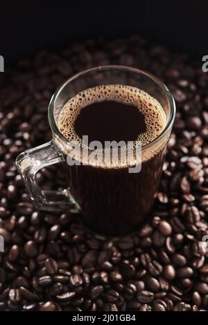 Anyone looking for a tall, dark and rich cuppa. Closeup shot of a cup of black coffee surrounded by coffee beans. Stock Photo