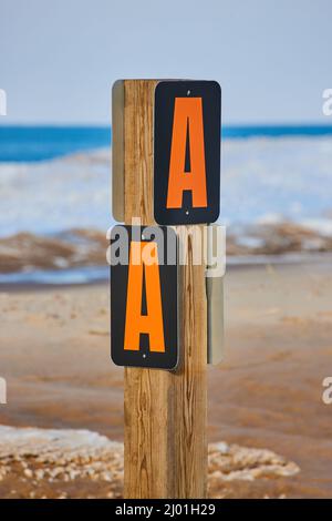 Signpost marker AA on sandy beach in winter with layer of snow and ice Stock Photo