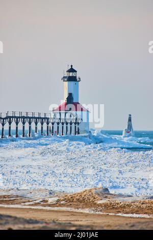 Winter view of red and white lighthouse on beach covered in ice Stock Photo