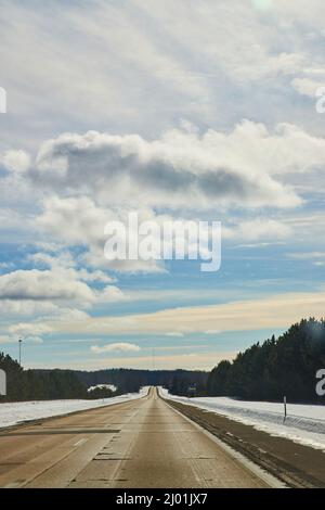 Open and empty highway road in winter with snow, blue sky, and white clouds Stock Photo