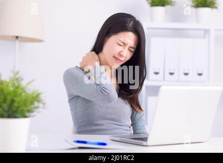 Young woman sitting at desk in front of laptop, touch neck feels pain Stock Photo
