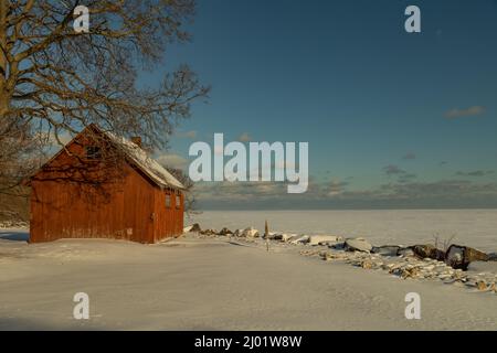 Red barn with icicles hanging down overlooking the frozen Lake Erie covered in snow during the winter Stock Photo