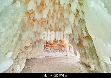 Ice cavern covered in small icicles and frozen lake on the ground Stock Photo
