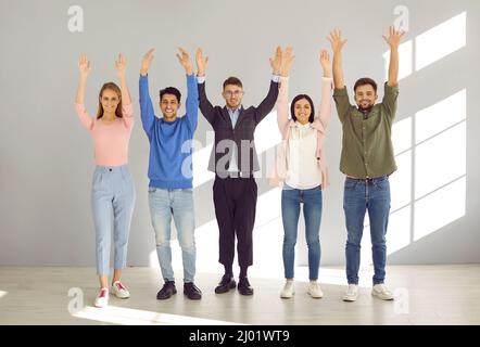 Portrait of cheerful young people standing in row with arms raised and smiling in front of camera. Stock Photo