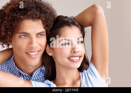 Lost in love.... Studio shot of a romantic young couple holding each other and looking away. Stock Photo