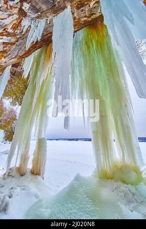 Frozen lake in winter with cave and hanging green icicles Stock Photo