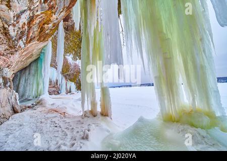 Thick icicle waterfalls of green and blue on rocks next to frozen lake Stock Photo