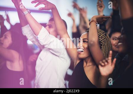 Thats my favourite song. Cropped shot of an attractive young woman cheering while standing in the crowd at a concert at night. Stock Photo