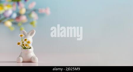 Easter white hare with a bouquet of daisies on a blue floral background. The concept of spring and Easter. Copy space. Stock Photo