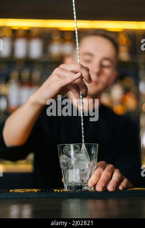 the barman holds a metal spoon with ice cubes in his hand and