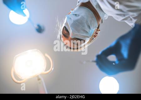 Just remain calm and Ill do the rest. Low angle shot of a focused young female dentist wearing a surgical mask while attempting to work on a patients Stock Photo