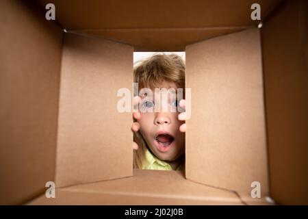 Kid opening package. Child boy age 6 year opening a carton box and looking inside, unpacking concept, surprise unboxing. Stock Photo
