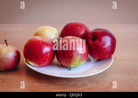 Red apples on a white plate on a wooden table. Stock Photo