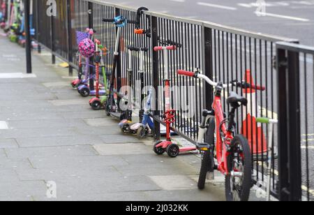 London, England, UK. Children's scooters chained to railings outside a primary school Stock Photo