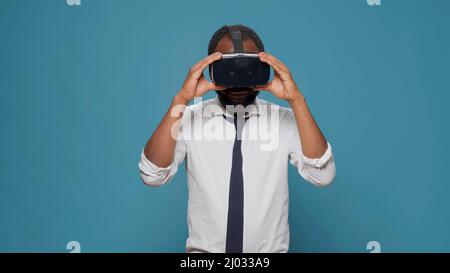 Young man wearing virtual reality glasses in front of camera, enjoying visual 3d simulation experience. Businessman using vr headset to play with innovative tech and futuristic vision. Stock Photo