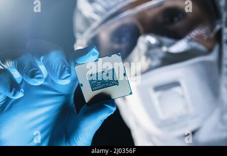 Ultra Modern Electronic Manufacturing Factory, Engineer in Sterile Coverall Holds Microchip with Gloves and Examines it Stock Photo