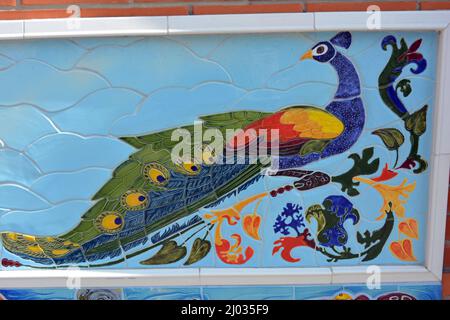Beautiful bright peacock pattern made of colored porcelain and faience slabs, porcelain mosaic. Colorful ceramic mosaic on the wall of the building. Stock Photo