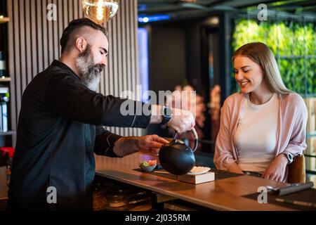Sushi master is serving sushi meal to cheerful young woman at sushi restaurant. Stock Photo