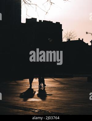 Two people walking at the sunset in the shadows with the building in background Stock Photo