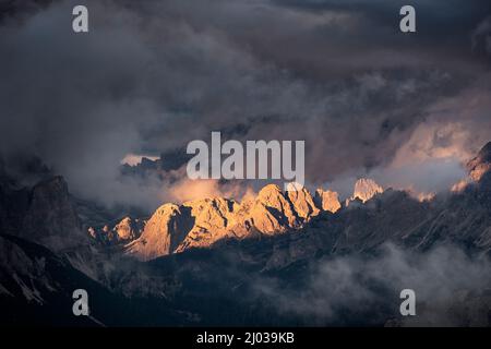 Light rays hitting Dolomites mountain peaks at sunset, surrounded by low clouds and mist, Cortina d'Ampezzo, Dolomites, Veneto, Italy, Europe Stock Photo