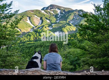 A girl sitting beside her border collie dog staring at a mountain landscape of Cusna Mountain, Emilia Romagna, Italy, Europe Stock Photo