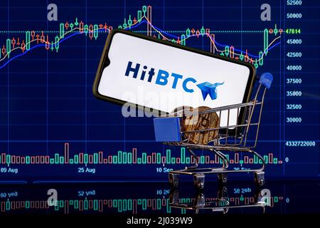 A smartphone with the HitBTC logo in shopping cart on the background of the live trading webpage. HitBTC dashboard. Stock Photo