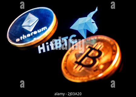 HitBTC logo on smartphone screen against the background of the main cryptocurrencies. Stock Photo