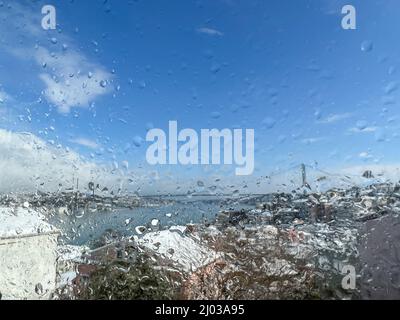 raindrops, raindrops on windowpane over blurred sky and city view under snow. water drops on window against blur background  or surface with houses wh Stock Photo