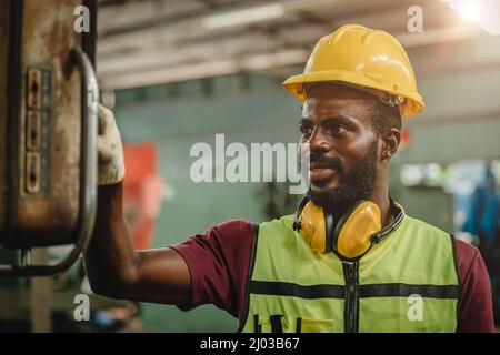 Black African professional worker working in heavy industry factory wearing engineer suit and helmet for safety.worker operating machine. Stock Photo