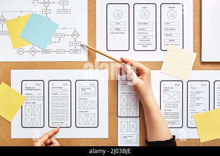 Web UX designer working on mobile responsive website. Flat lay image of numerous app wireframe sketches and user flow over product designer desk. Stock Photo