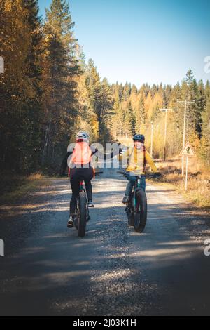 Cycling friends greet each other as they meet on a dirt road in Vuokatti area, Kainuu, Finland. Female cyclists in sportswear on fat bikes. Stock Photo