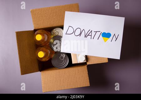 Donation for people from Ukraine. Food donations boxes with grocery products and white card with text Donation on gray background. Top view. Stock Photo