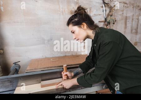 Side view of brunette woodworker using jointer machine Stock Photo