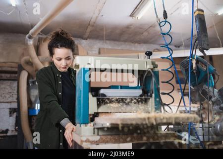 Woodworker using thickness planer while working in workshop Stock Photo
