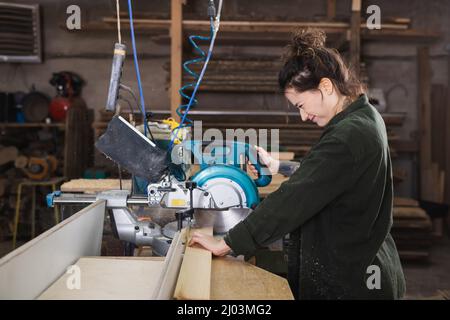 Side view of smiling carpenter using miter saw in workshop Stock Photo