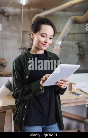 Positive furniture designer using digital tablet near protective visor in workshop Stock Photo