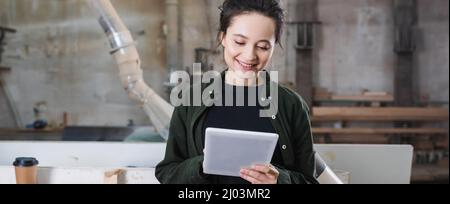Young furniture designer smiling while using digital tablet in workshop, banner Stock Photo