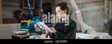 Young carpenter using digital tablet in workshop, banner Stock Photo