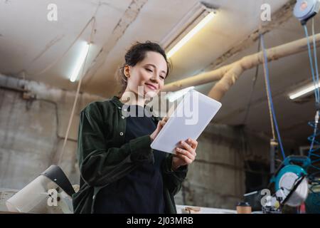 Low angle view of young carpenter using digital tablet near safety visor in workshop Stock Photo