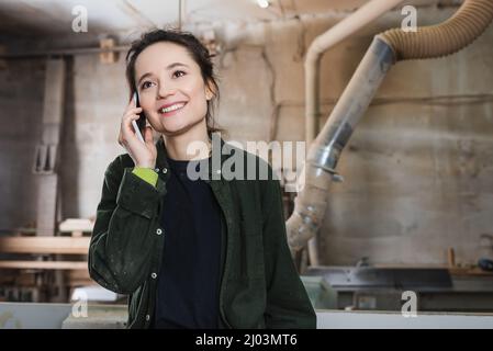 Happy woodworker talking on mobile phone in workshop Stock Photo