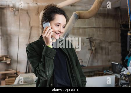Cheerful furniture designer talking on cellphone in workshop Stock Photo