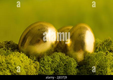 Three gold painted easter eggs on a mossy green background Stock Photo