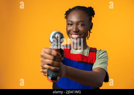 Black African American female model in uniform holding a screwdriver repair tool against yellow background Stock Photo