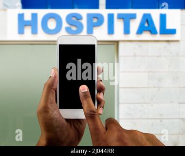 Hand holding mobile smart phone with blank screen next hospital building and with copy space Stock Photo