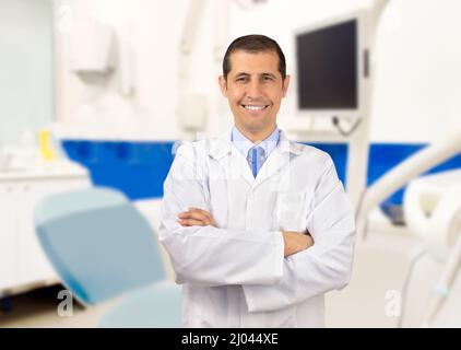 A male dentist standing next to his desk with his arms folded and smiling at the camera Stock Photo