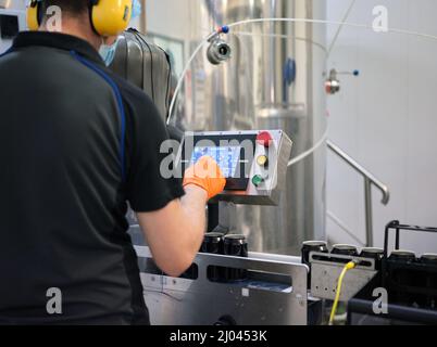 Worker with protective gear using an electronic device of a machine in a brewery Stock Photo