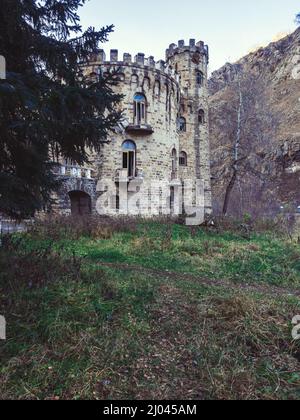 On a clearing in mountain forest valley stands an abandoned castle with broken windows and ruined balconies. Stock Photo