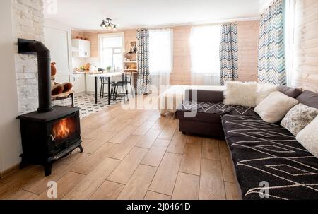Interior of a bright studio room with a Scandinavian style fireplace in a private house, where the living room is combined with kitchen. Stock Photo