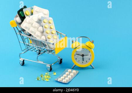 Pills in shopping cart and yellow clock on blue background Stock Photo